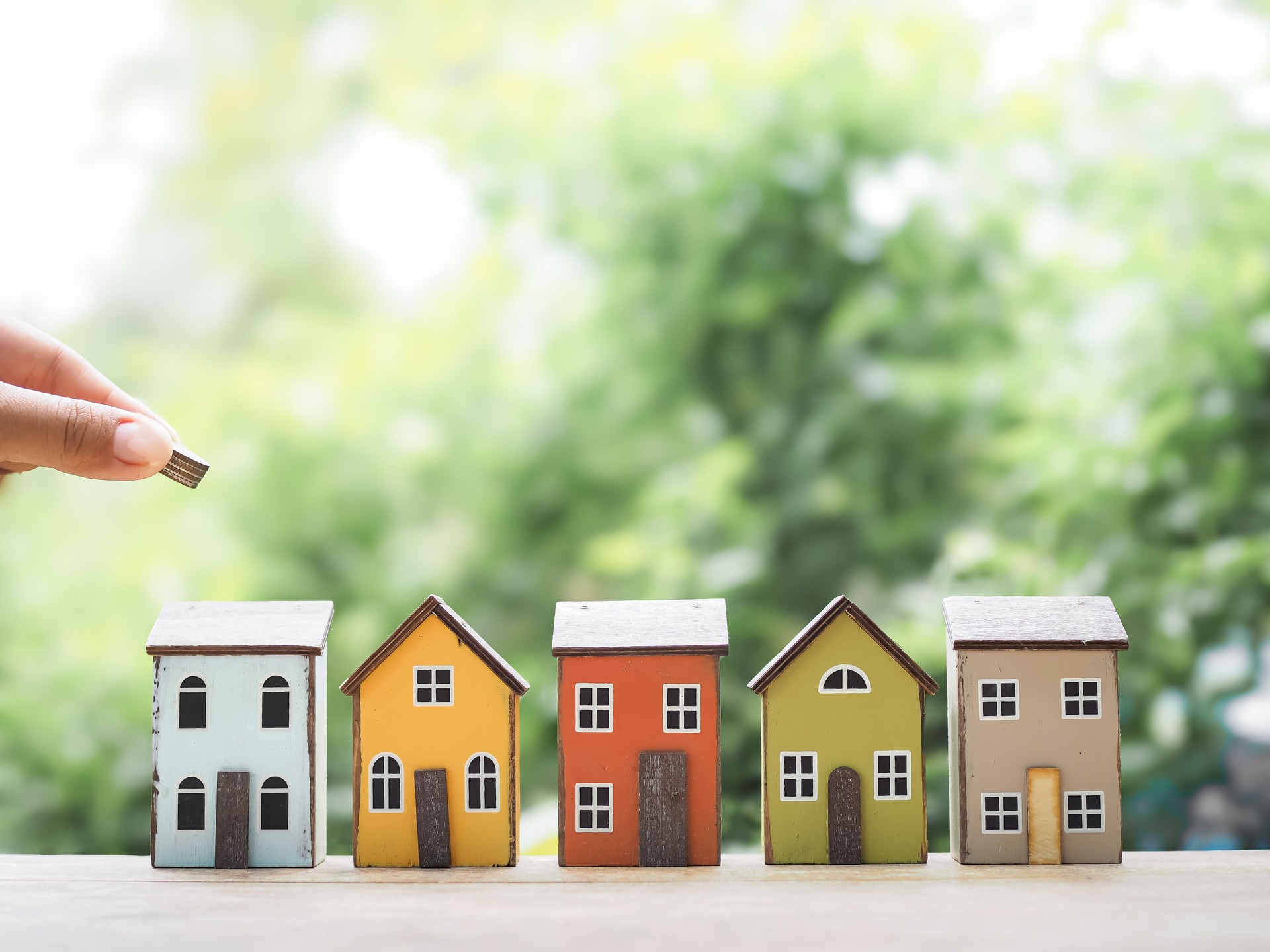 Close up hand putting coin with miniature house. The concept of saving money for house, Property investment, House mortgage, Real estate.